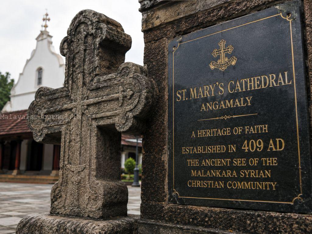 A close-up shot of the ancient stone cross and the historical plaque at the entrance of St. Mary's Cathedral Angamaly