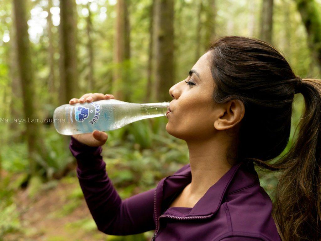a woman drinking a bottle of water in the woods