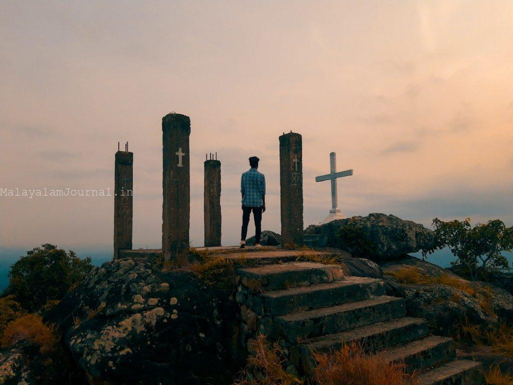 a man standing on top of a hill next to a cross