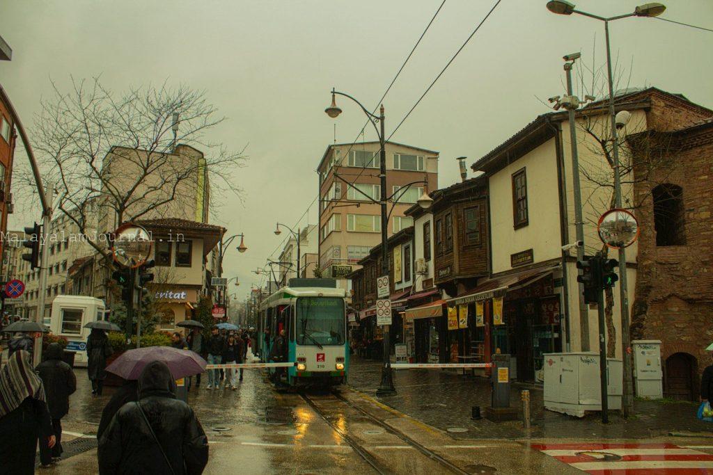 A tram travels down a wet street in a city.